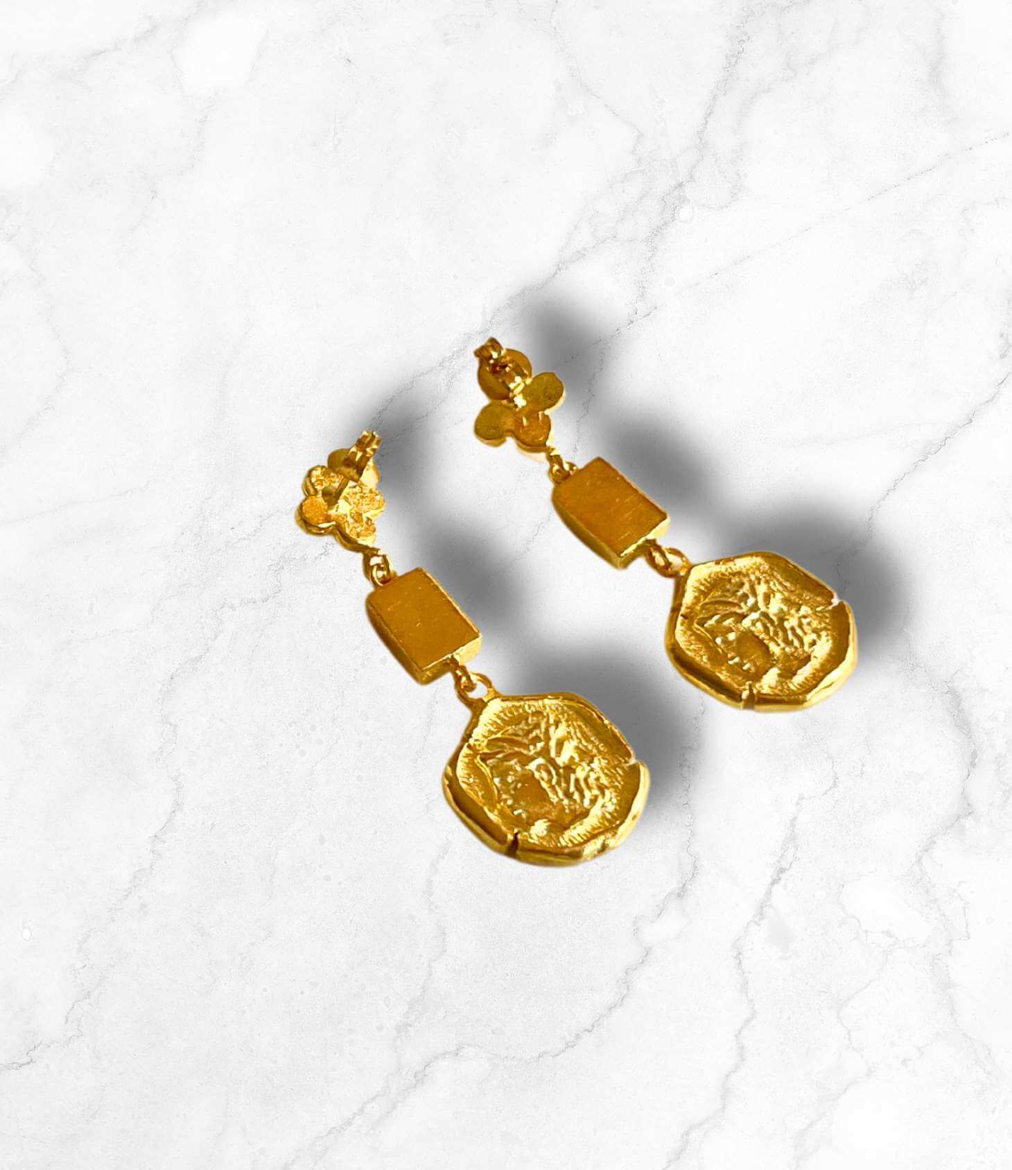 Elegant gold disc earrings with a unique geometric design on a marble background.