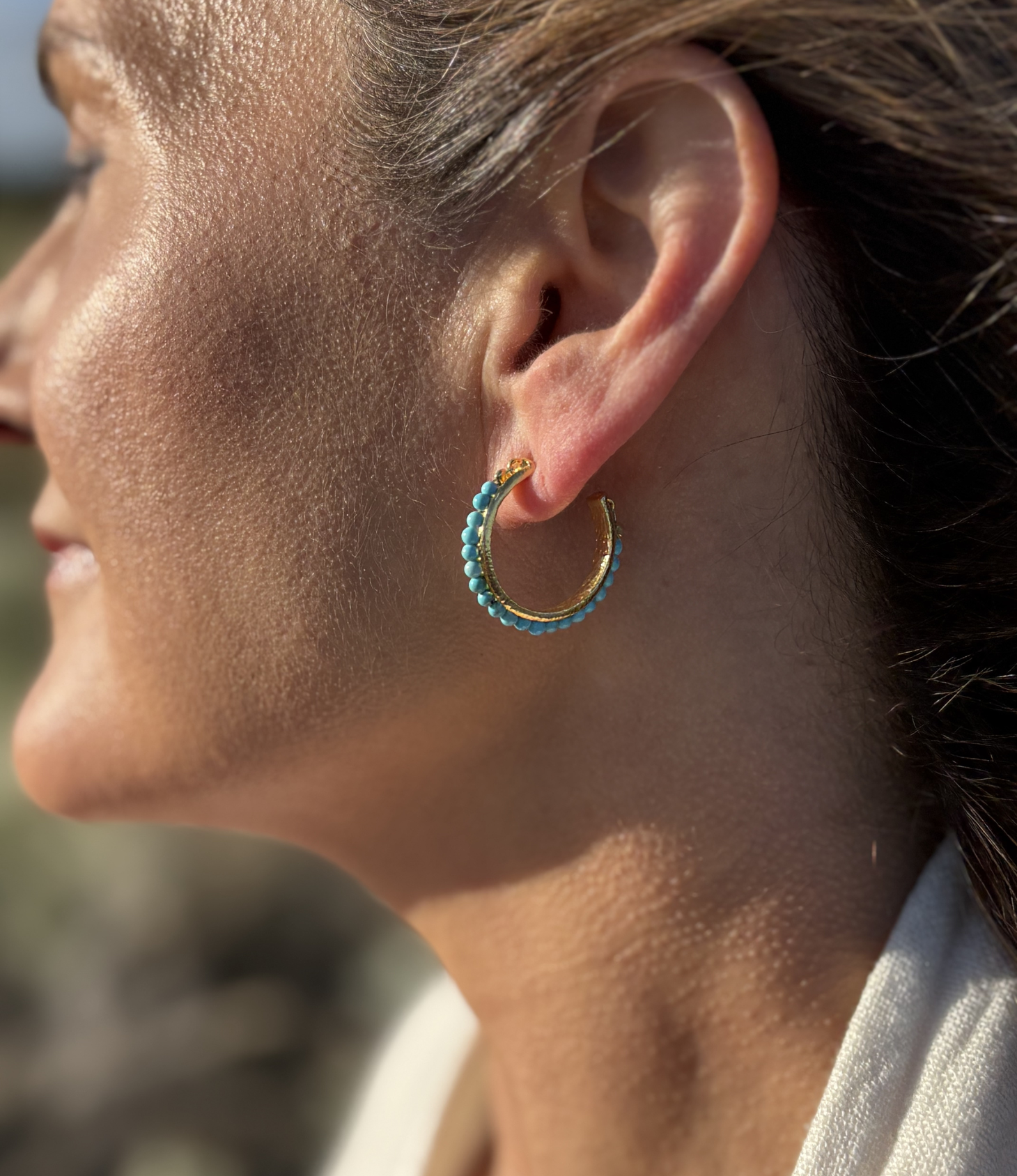 Close-up of a woman wearing turquoise hoop earrings made of 18k gold plated sterling silver.