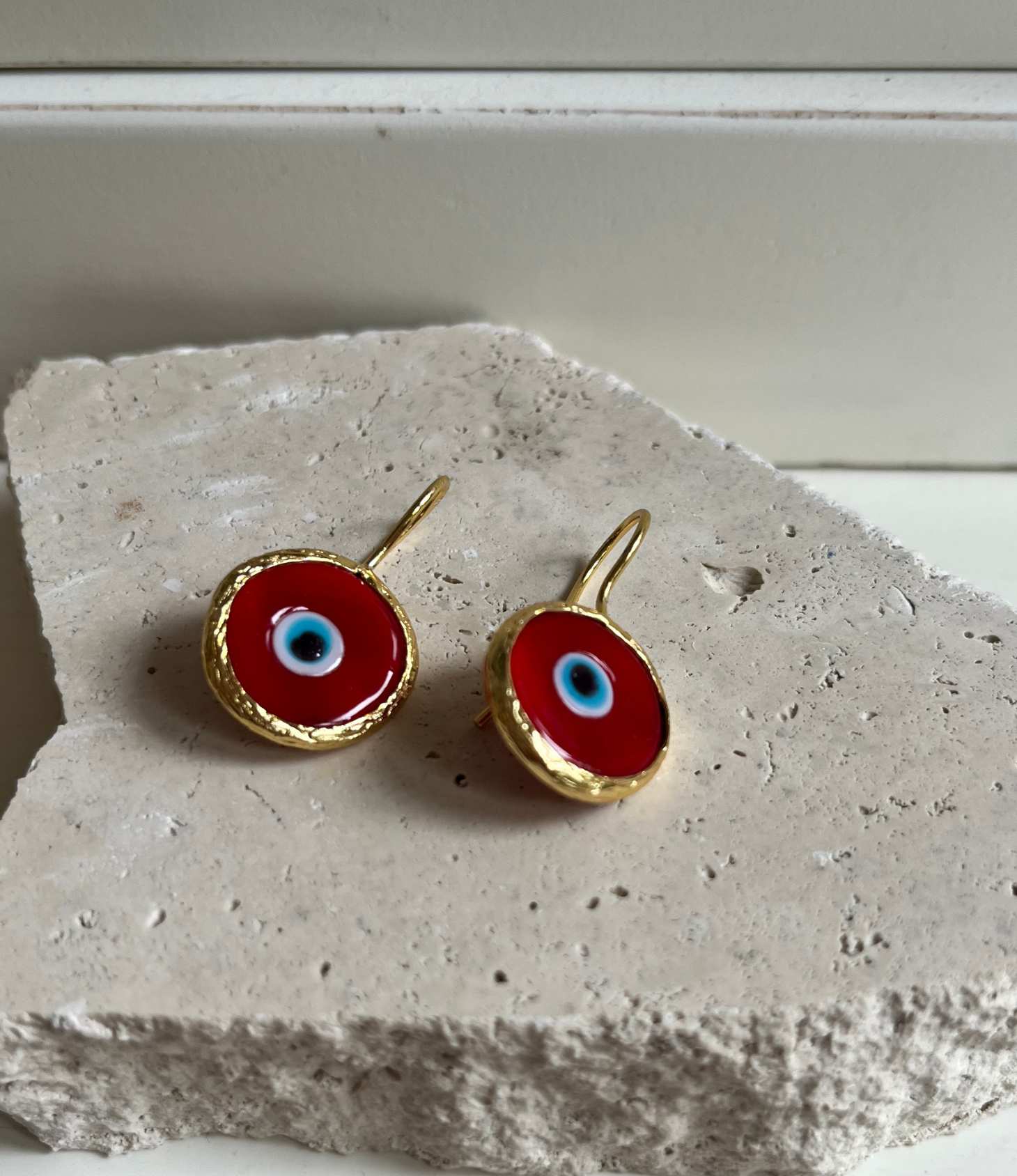 Red evil eye earrings with gold detailing displayed on a natural stone surface