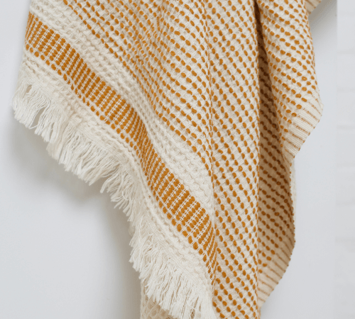 Close-up of a Turkish beach towel featuring a textured pattern in cream and mustard yellow with fringed edges.