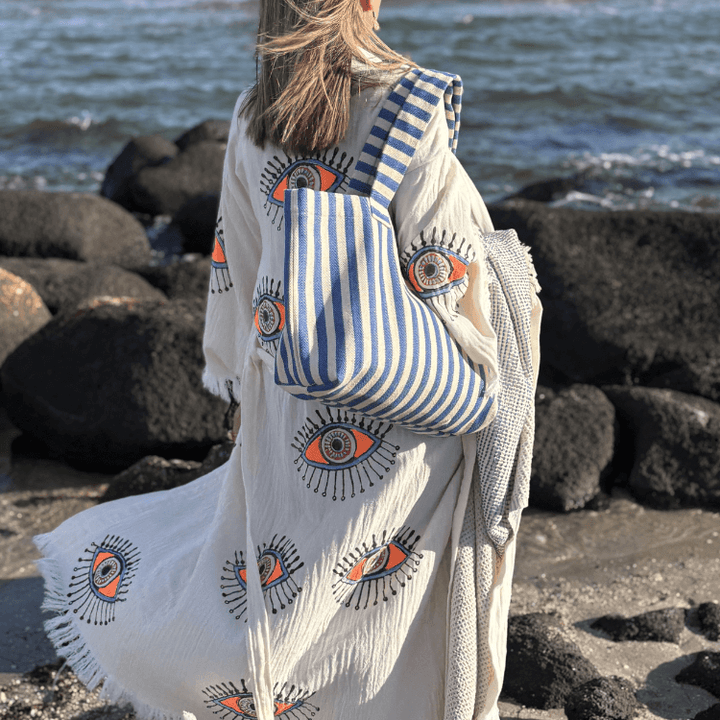 model wearing evil eye robe with beach summer tote and beach towel