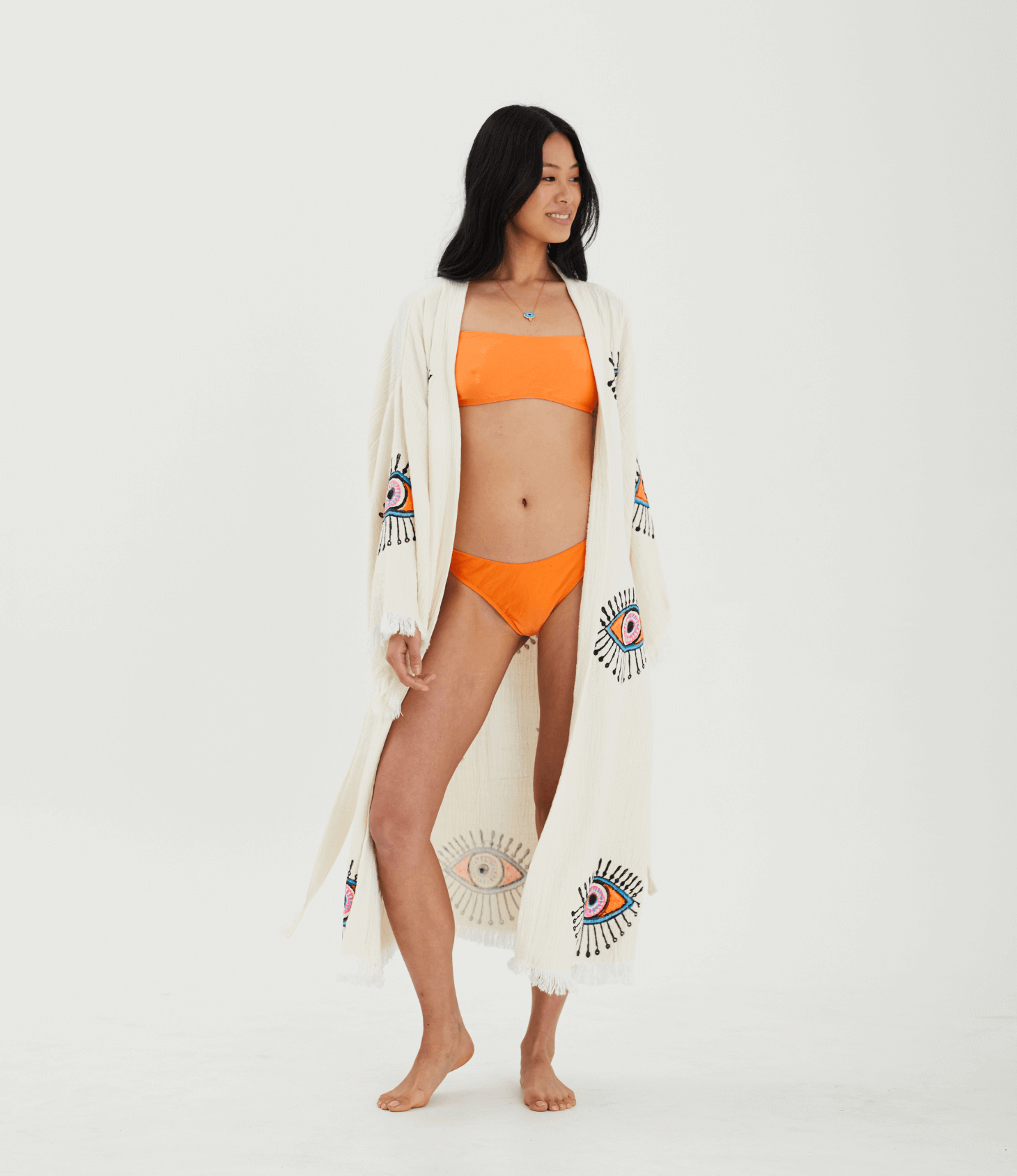Model wearing an Evil Eye Robe over an orange bikini, showcasing its elegant design and vibrant patterns.
