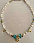 Necklace with white beads, gold accents, and turquoise elements on a light gray background