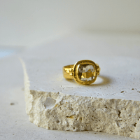 Green Amethyst Gold Ring resting on a stone surface, showcasing its luxurious design and sparkling gemstone.
