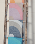 Colorful towels in pastel shades displayed on a rustic ladder against a white wall, showcasing vibrant wave patterns.