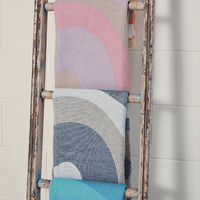 Colorful towels in pastel shades displayed on a rustic ladder against a white wall, showcasing vibrant wave patterns.