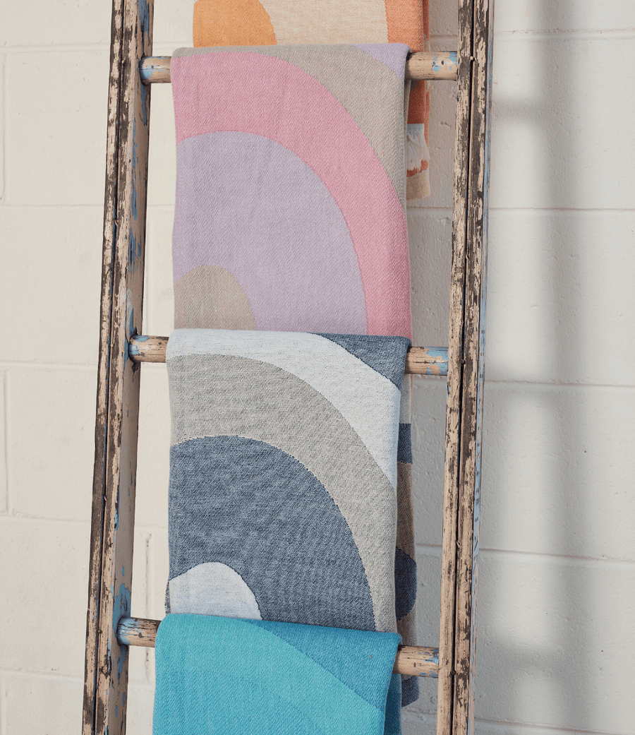 Colorful towels in pastel shades displayed on a rustic ladder against a white wall, showcasing vibrant wave patterns.