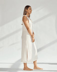 Side view of a woman in a soft cotton dress with tied straps and leg slits against a light background.