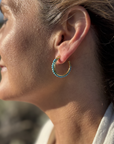 Close-up of a woman wearing turquoise hoop earrings made of 18k gold plated sterling silver.