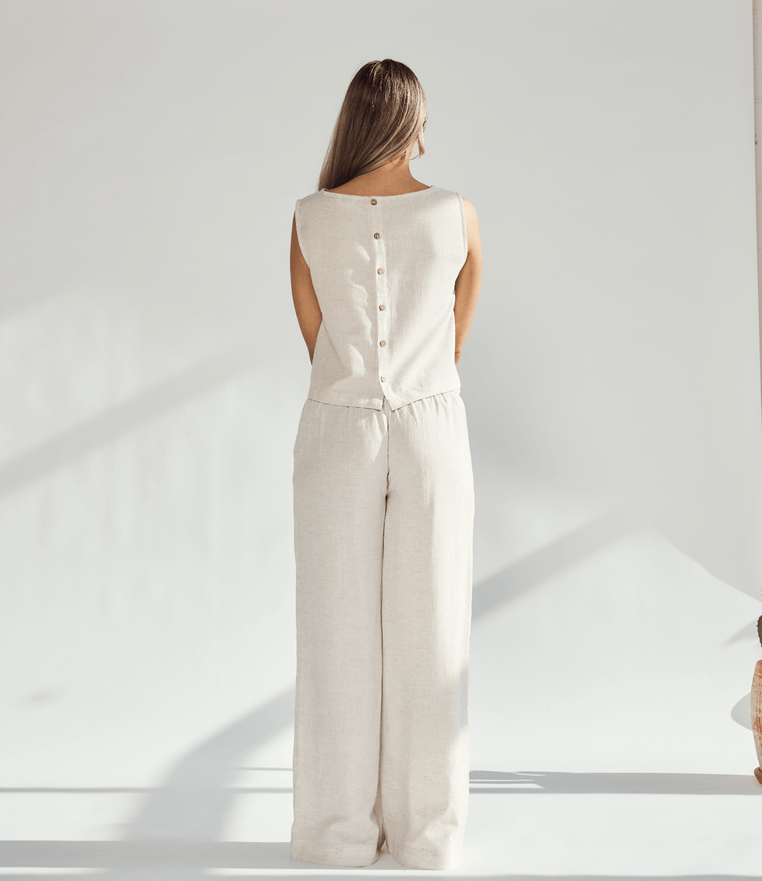 Back view of a woman in a beige linen wide leg and crop top set, showcasing buttons and a chic silhouette.