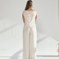 Back view of a woman in a beige linen wide leg and crop top set, showcasing buttons and a chic silhouette.