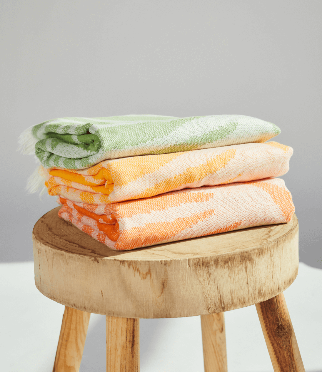 Three Radiance Turkish Beach Towels with vibrant sunburst patterns stacked on a wooden stool.