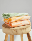 Three Radiance Turkish Beach Towels with vibrant sunburst patterns stacked on a wooden stool.