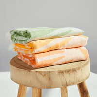 Three Radiance Turkish Beach Towels with vibrant sunburst patterns stacked on a wooden stool.