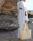 Woman wearing a Leopard Print Muslin Cotton Robe with a yellow striped tote bag at the beach.