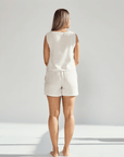 Woman wearing a white sleeveless top and shorts against a plain background
