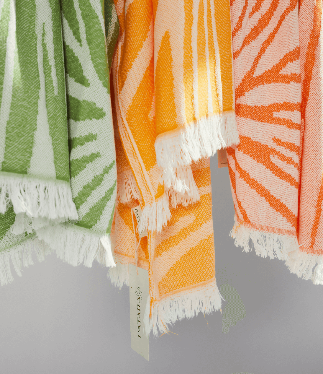 Colorful Radiance Turkish Beach Towels in orange, green, and peach with sunburst pattern and fringed edges.