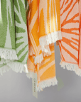 Colorful Radiance Turkish Beach Towels in orange, green, and peach with sunburst pattern and fringed edges.