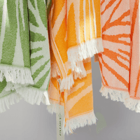Colorful Radiance Turkish Beach Towels in orange, green, and peach with sunburst pattern and fringed edges.