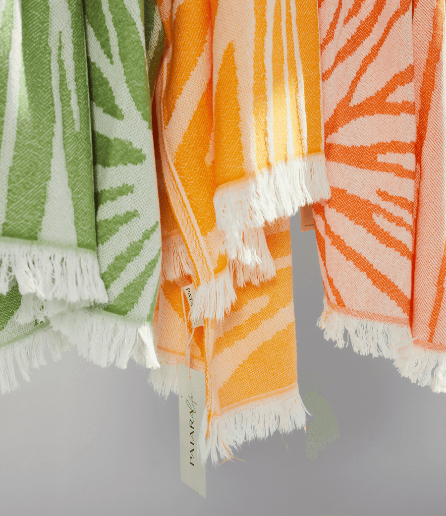 Colorful Radiance Turkish Beach Towels in orange, green, and peach with sunburst pattern and fringed edges.