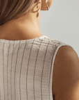 Close-up of a person wearing a sleeveless top with black pinstripes on a neutral background