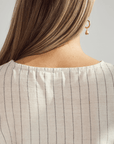 Close-up of a person wearing a beige pinstripe top with a plain background