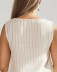 Close-up of a person wearing a beige sleeveless top with thin vertical stripes on a light gray background.