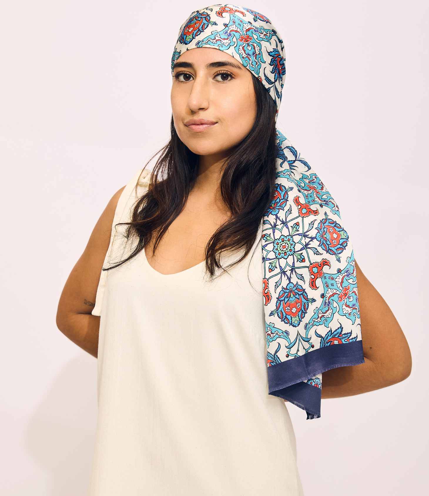 Woman wearing a patterned headscarf on a plain background