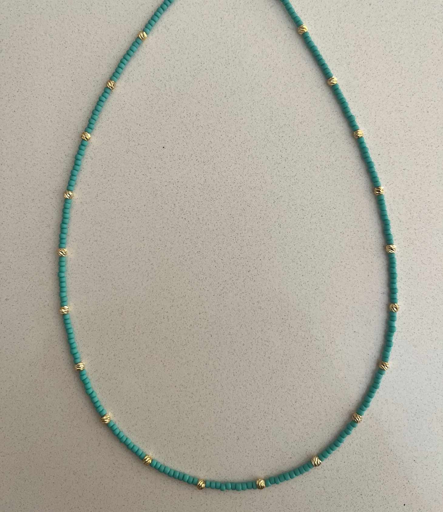 Turquoise beaded necklace with gold accents on a light gray background