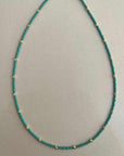 Turquoise beaded necklace with gold accents on a light gray background