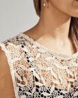 Close-up of a person wearing a white lace top against a neutral background
