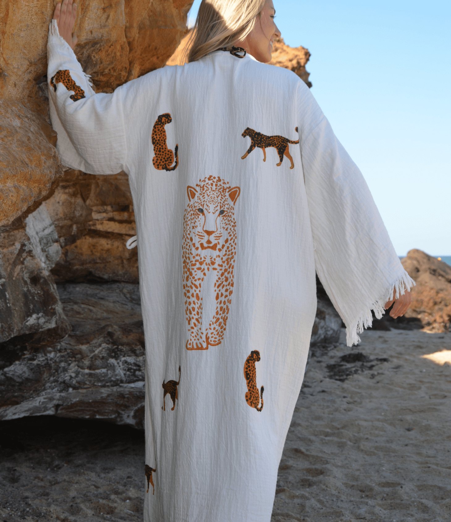 Woman wearing a leopard print muslin cotton robe on a beach, showcasing intricate animal designs.