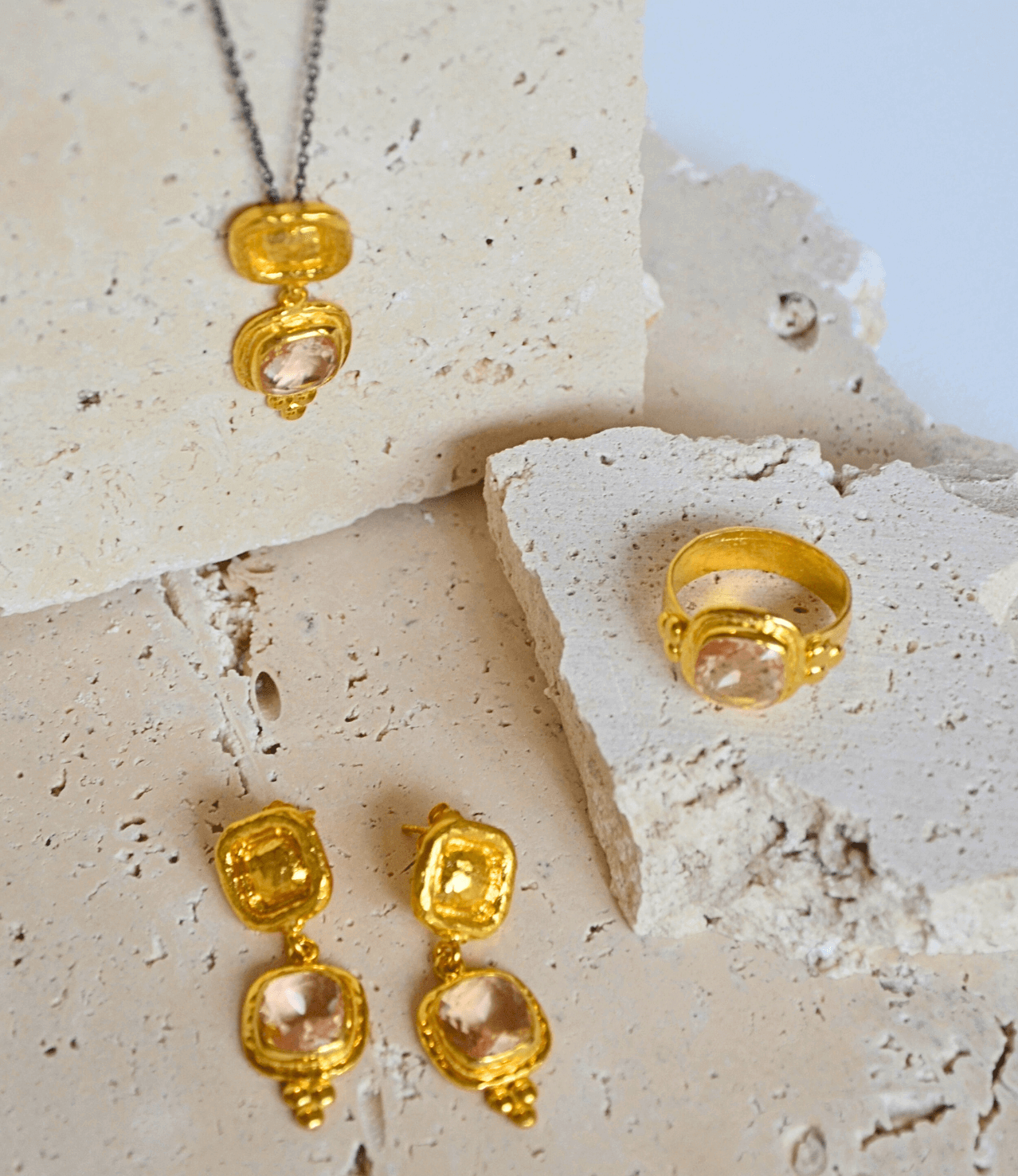 Gold jewelry set with pink gemstones on a textured stone surface.