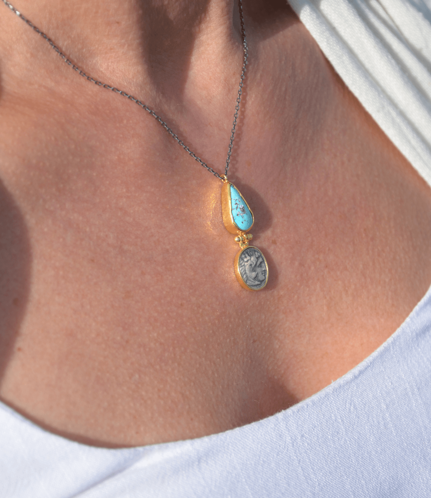 Close-up of a turquoise coin necklace featuring a diamond-shaped turquoise stone and an ancient Roman coin.