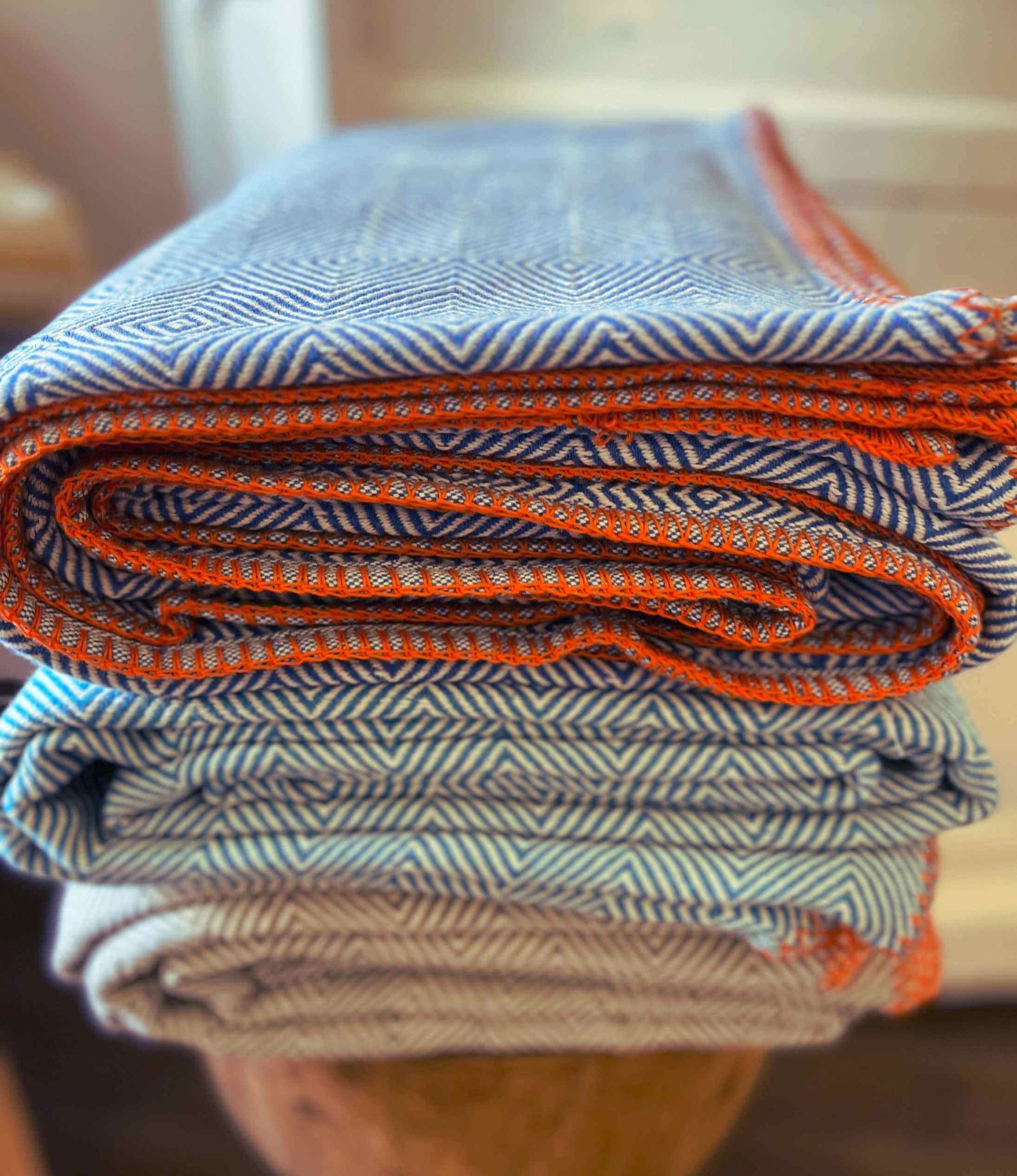 Stack of folded fabric with blue, orange, and beige patterns on a wooden surface.