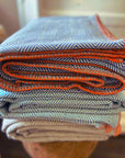 Stack of folded fabric with blue, orange, and beige patterns on a wooden surface.