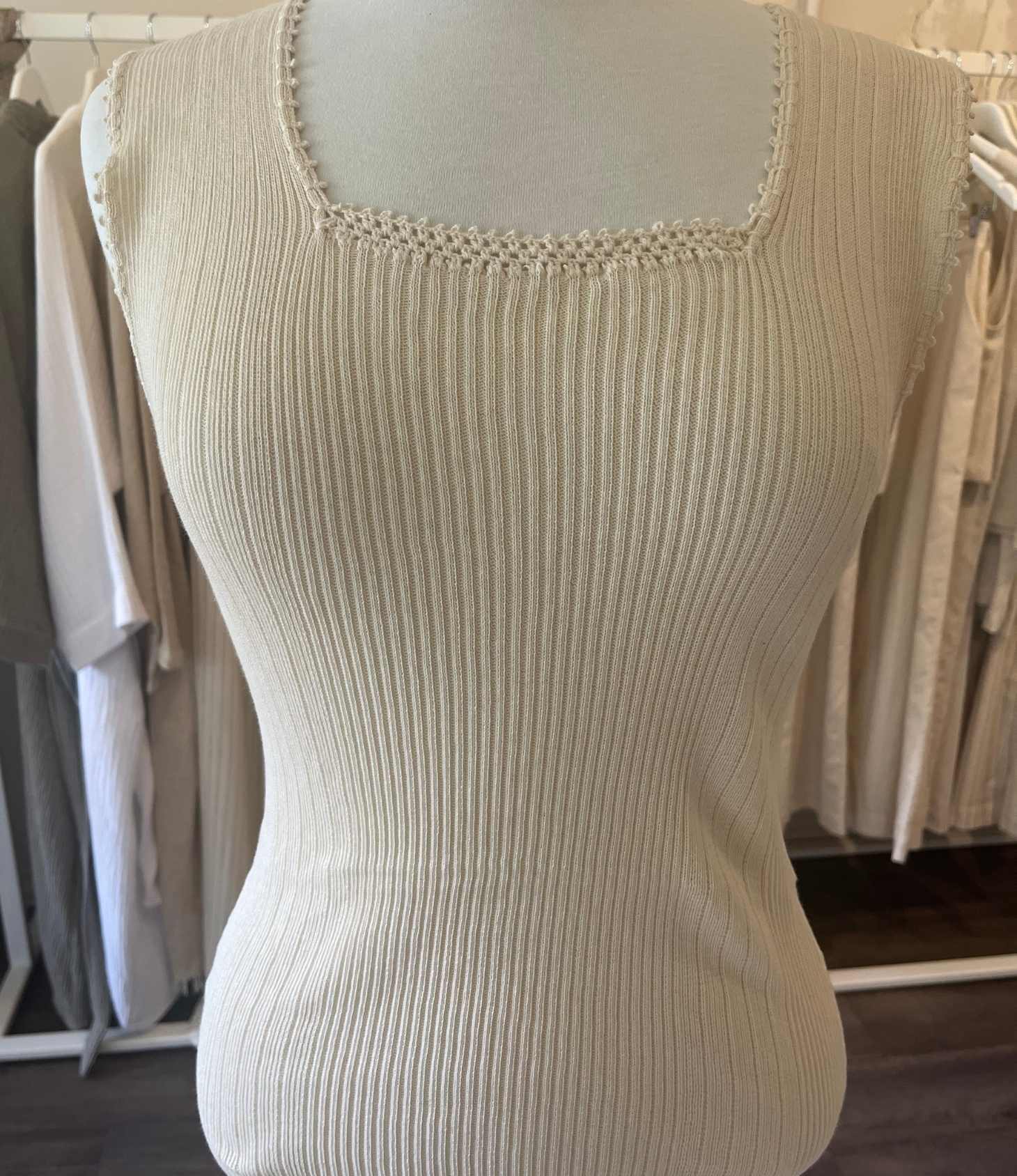 Beige ribbed tank top on a mannequin with a blurred clothing store background