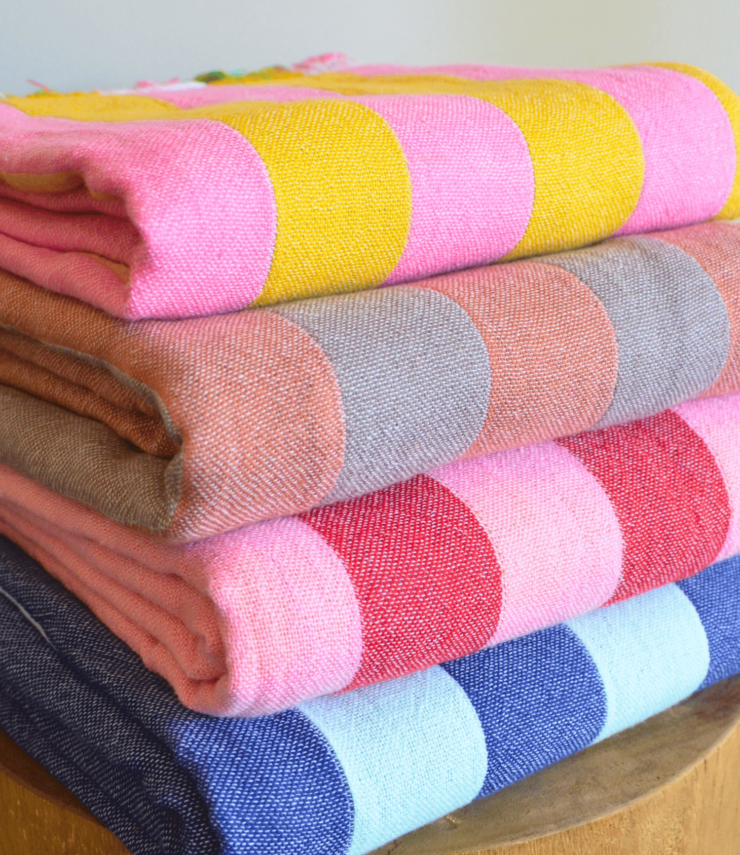Stack of colorful folded fabrics with circular patterns on a wooden surface.