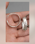 Enhanced detail shot of the Sculpted Silver Hoops pair in hand