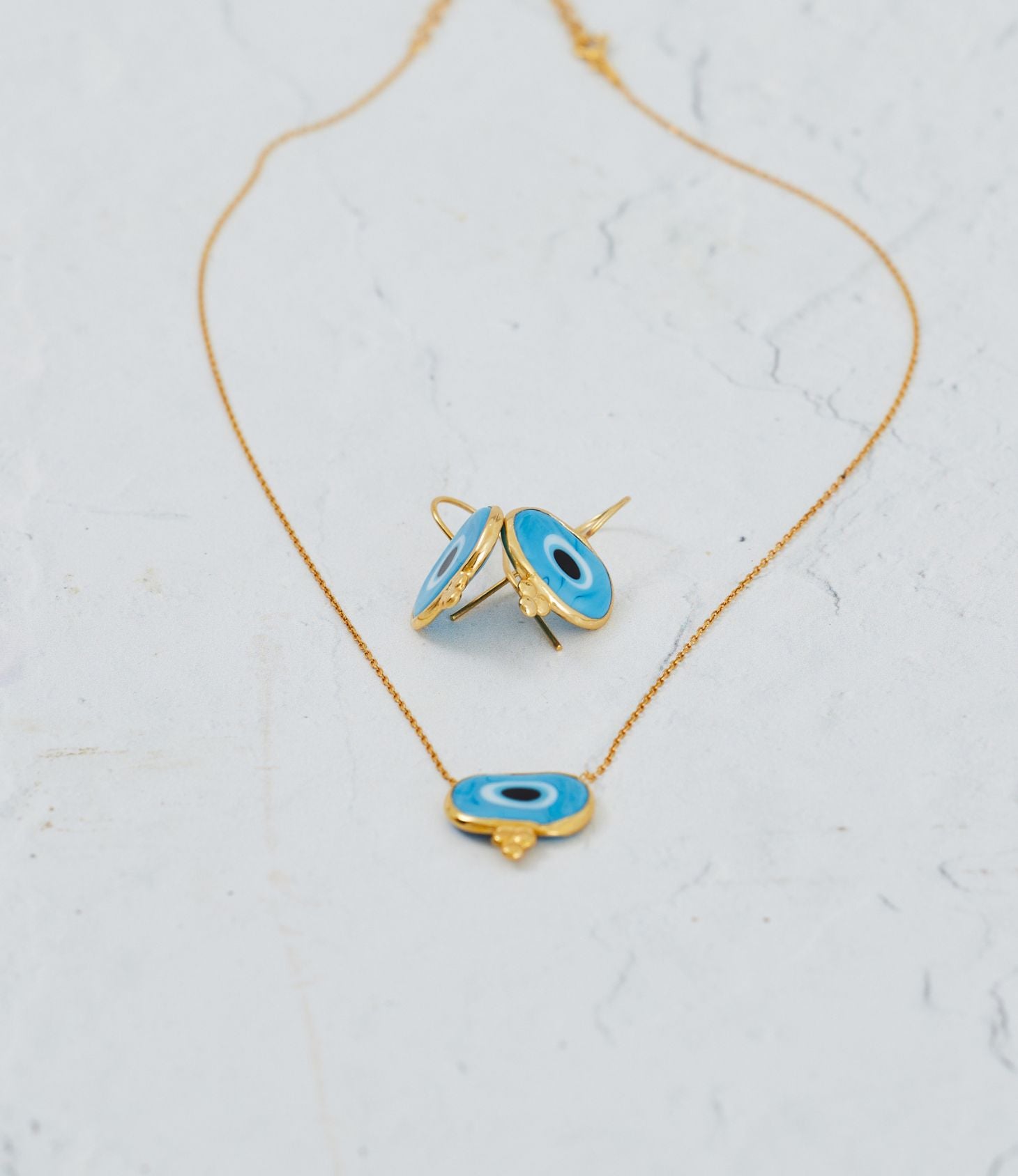 Gold necklace with blue evil eye pendants on a light gray background