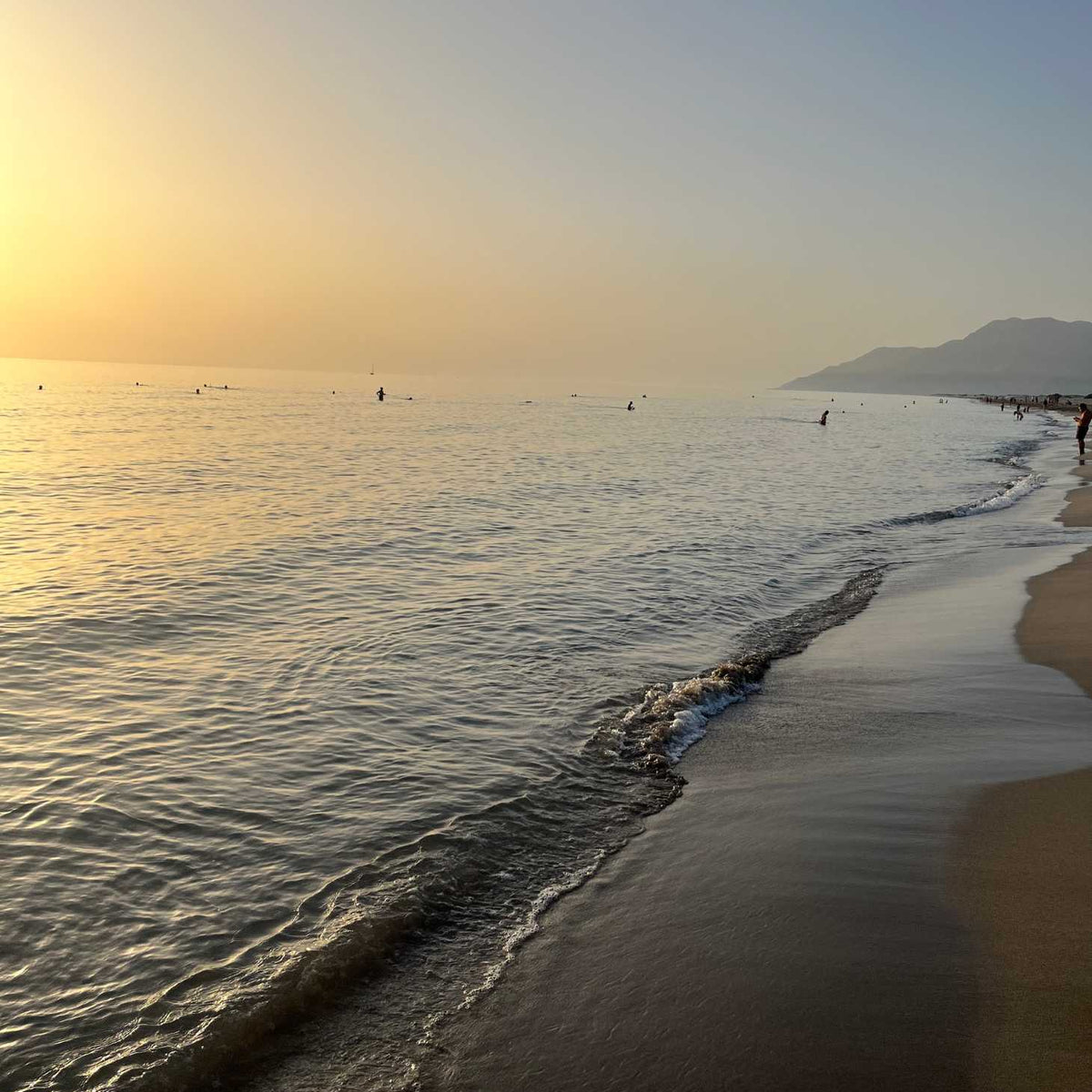 Sunset at a beach with gentle waves and a mountain in the distance.