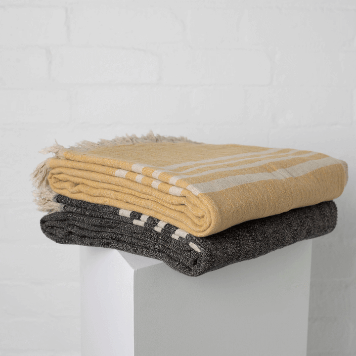 Stack of folded linen throws, one yellow and white striped, one black and white patterned, on a white surface.